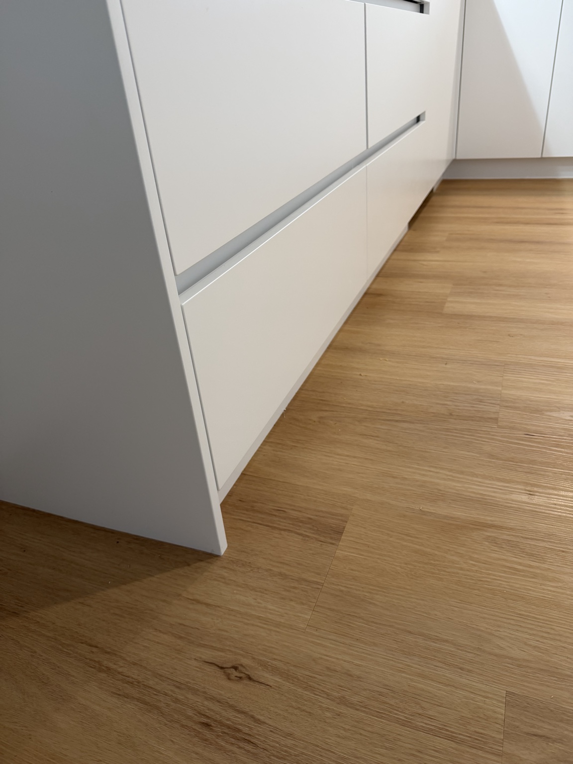 Close view of vinyl plank flooring beside white kitchen cabinetry